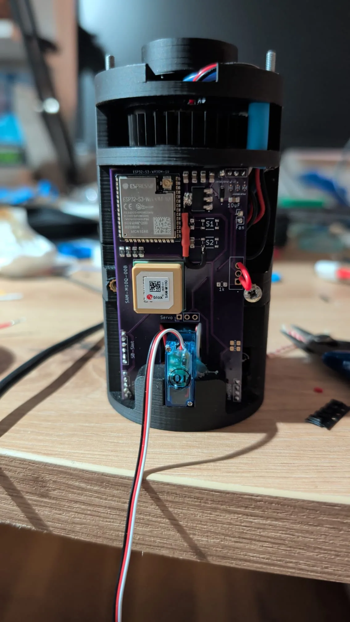 Der echte BioSat-CanSat: schwarzes 3D-gedrucktes Gehäuse mit violetter Platine, ESP32-S3- und GNSS-Modul, darunter das blaue Servo